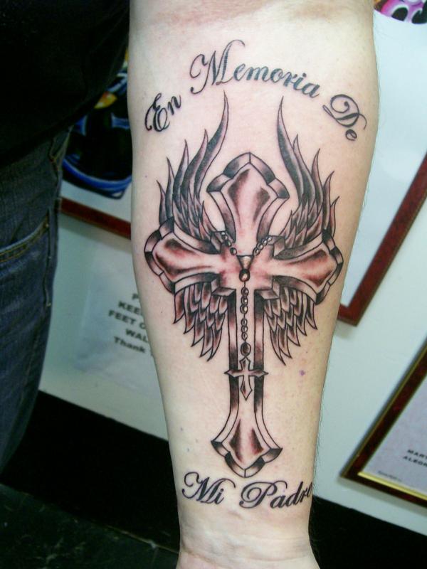Tatuagem de uma cruz sobre asas no braço