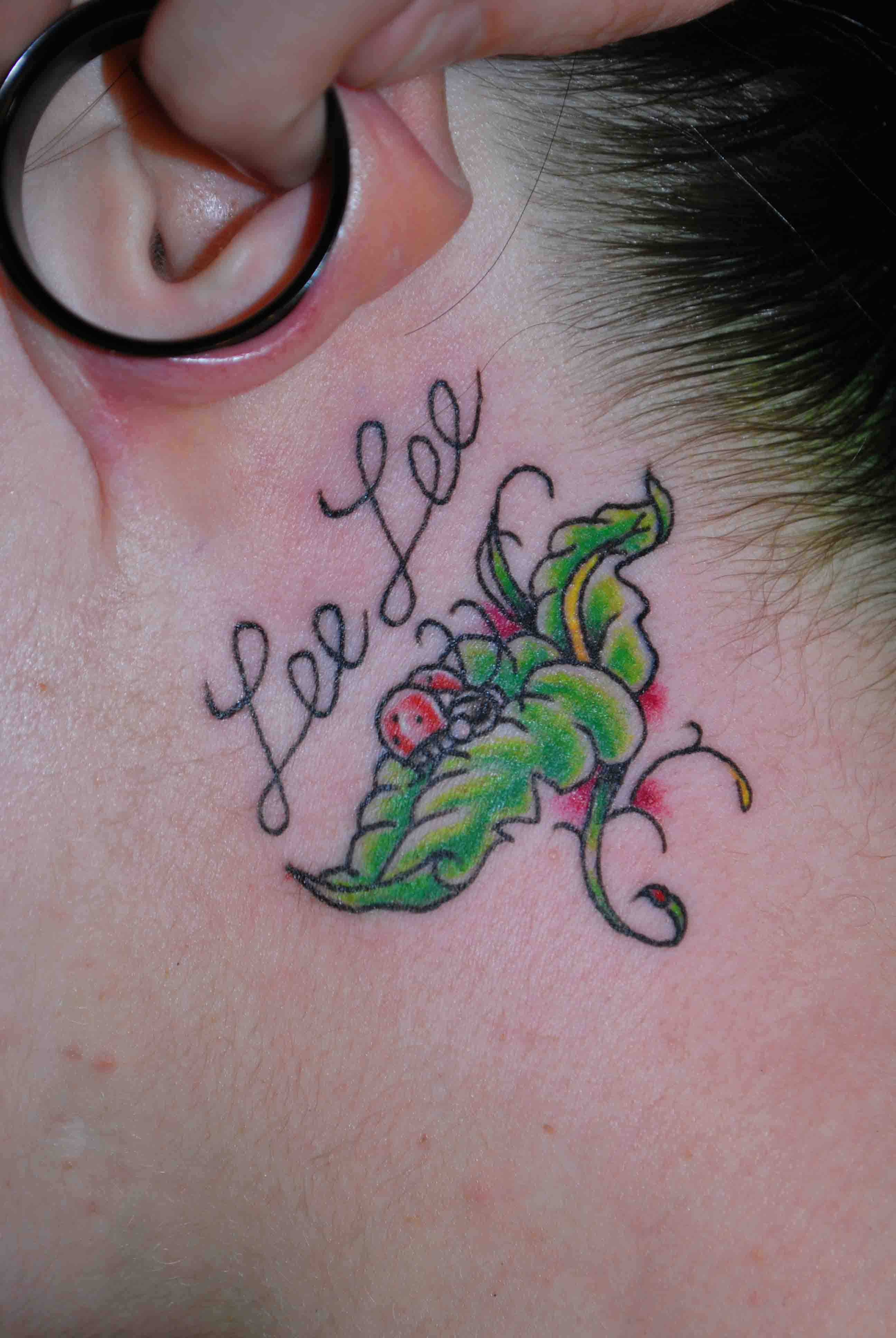 Name tattoo with flower design behind ear