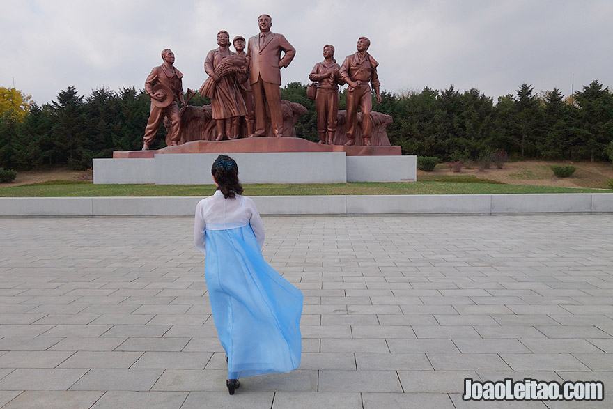 Woman with a traditional Korean blue dress and statues with the past leader Kim Il Sung.